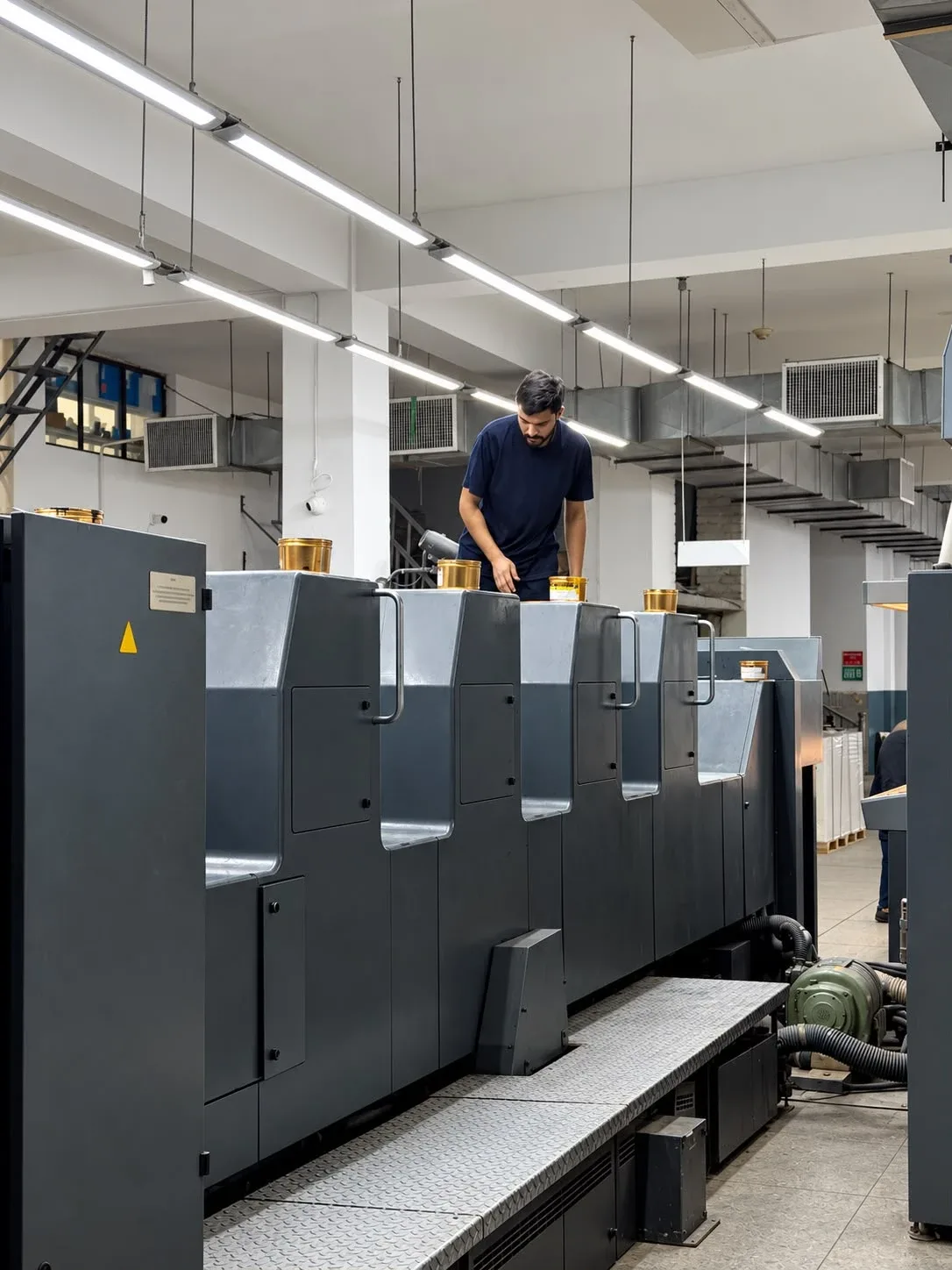 Press operator loading ink tins on top of the printing units.